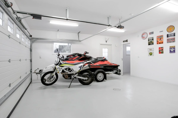 Rymligt och ljust garage med en motorcykel och en vattenskoter på släp, vita väggar och retro plåtskyltar