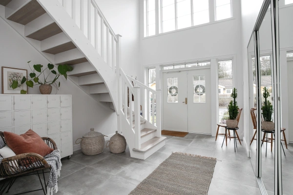 Ljus och rymlig entréhall med vit trappa, grått klinkergolv och spegelgarderob