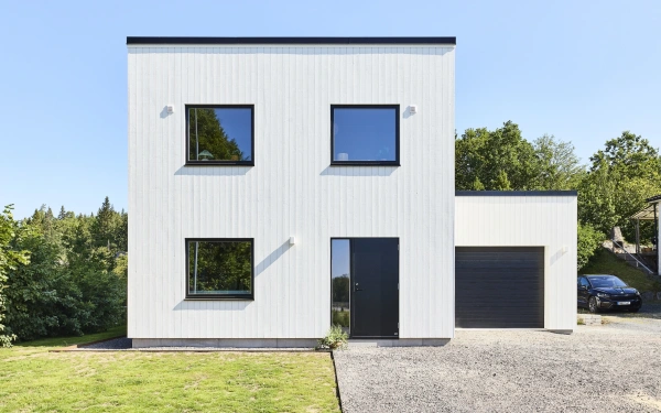 Modern tvåplansvilla med vit träfasad, svarta fönster och integrerat garage.