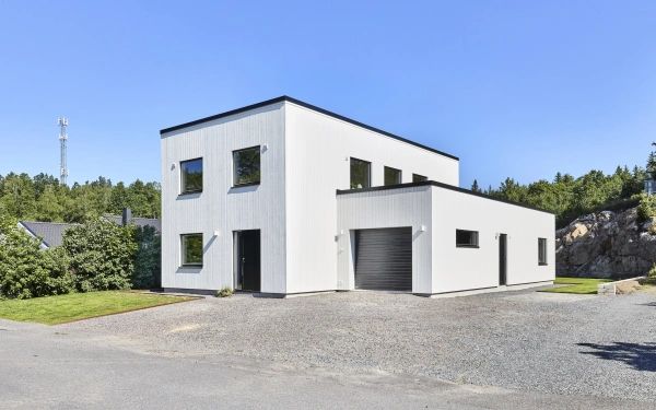 Modern tvåplansvilla med vit träfasad, svarta fönster och integrerat garage.