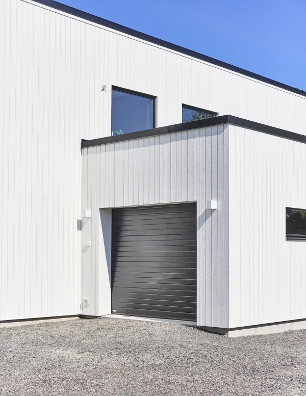 Detalj av vit träfasad med svart garageport, svarta fönster och plåtdetaljer.