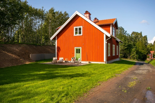 Rödmålat trähus med vita knutar, grön dörr och stensatt uteplats,