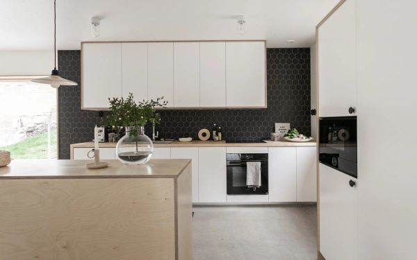 Modernt kök med vita skåpluckor, kanter i ljust trä, svart sexkantigt kakel och en köksö i plywood