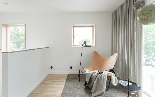 Ljus läshörna med fladdermusfåtölj i läder, mörk vävd matta, svart golvlampa och fönster med träram