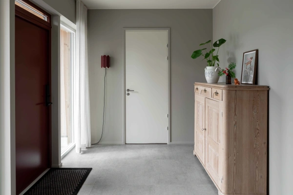 Ljus hall med grått klinkergolv, röd ytterdörr, en rustik träskänk och dämpade grå väggar
