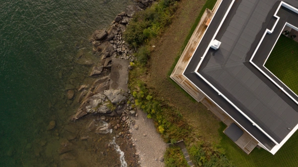 Flybild rakt ovandör ett modernt hus med strandtomt.