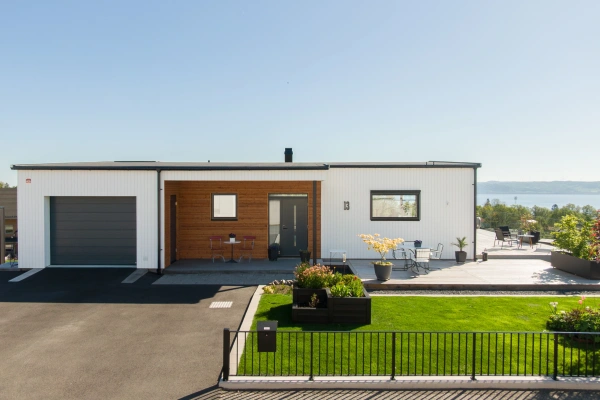Modern villa med vit träfasad, integrerat garage och uteplats med utsikt över vattnet.