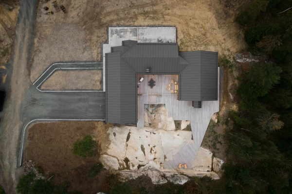Flygbild ovanifrån av en arkitektritad villa, anpassad efter en kuperad naturtomt med stora berghällar.