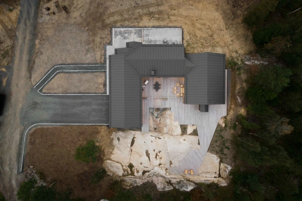 Flygbild ovanifrån av en arkitektritad villa, anpassad efter en kuperad naturtomt med stora berghällar.