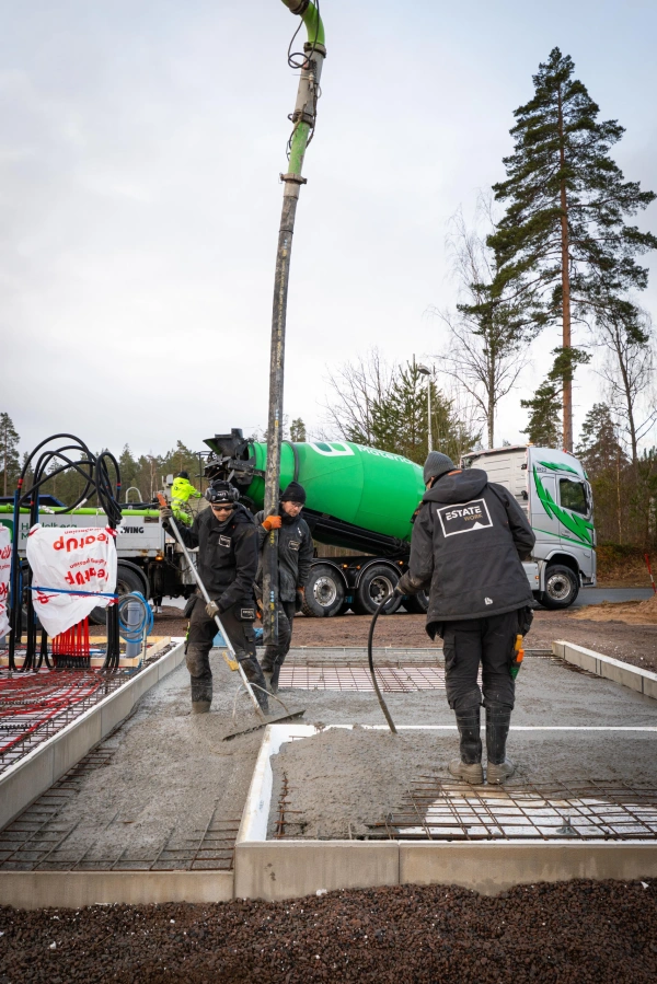 Byggarbetare gjuter en betongplatta med betongpump och betongbil på plats.